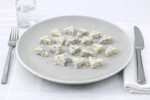 queso azul artesano en plato hondo con cubiertos y vaso de agua, ejemplo de porción moderada.
